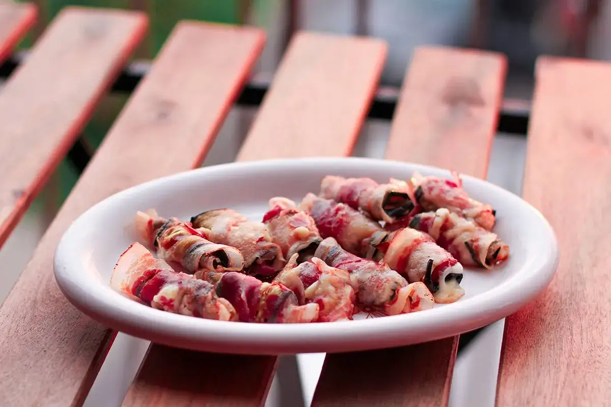 Ein Teller mit rohen Pancetta-Röllchen, bereit zum Grillen.