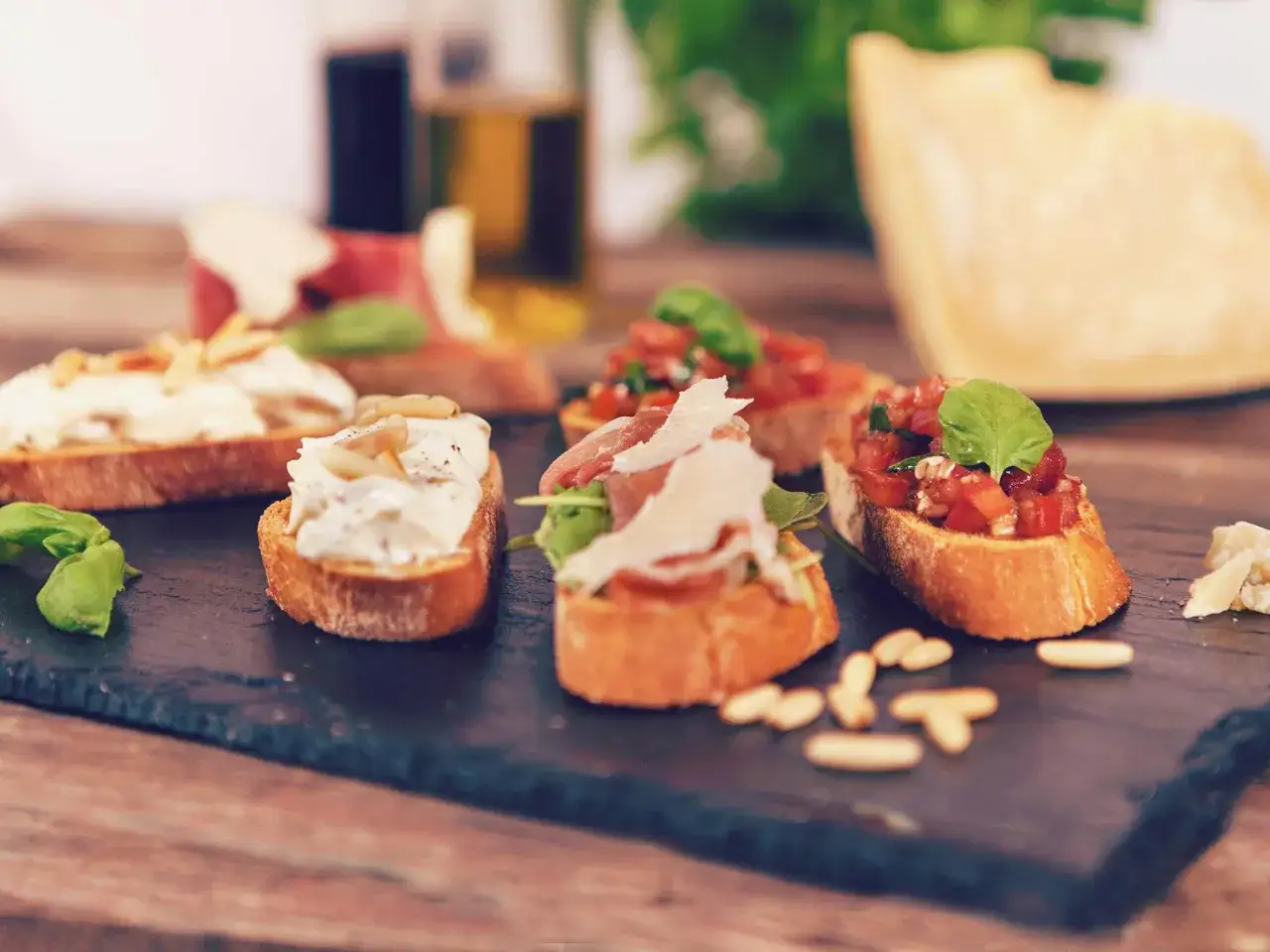 Verschiedene italienische Crostini mit Tomaten, Prosciutto und Käse, garniert mit Basilikum und Pinienkernen.