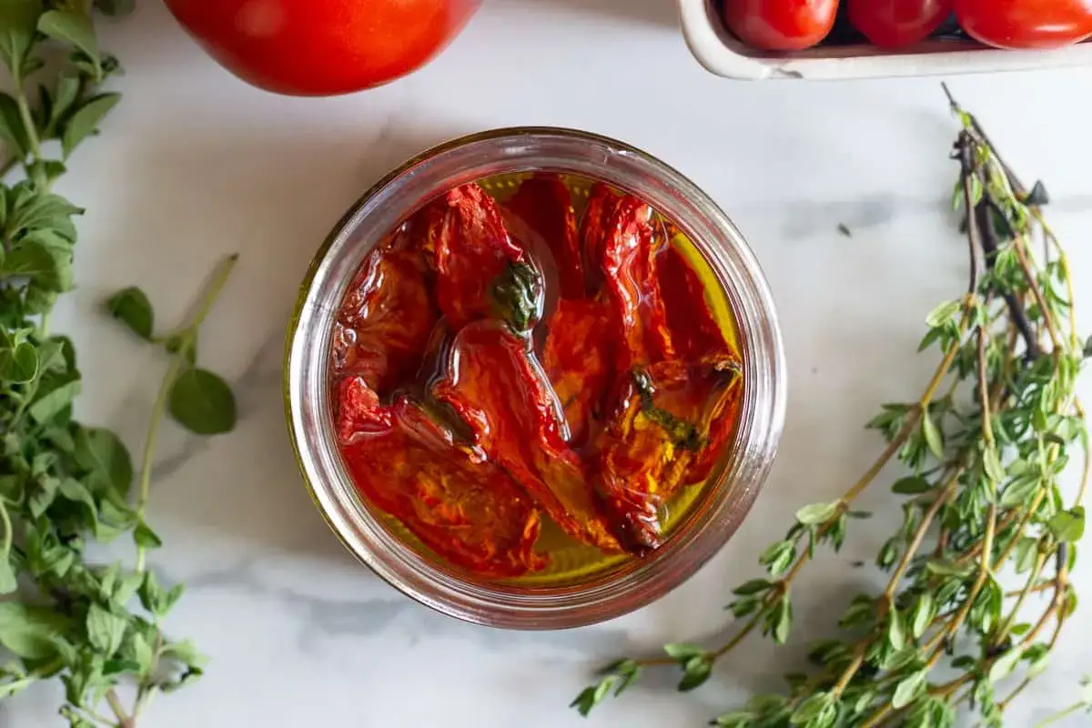 Ein Glas mit aromatischen pomodori secchi deutsch, umgeben von frischen Kräutern und Tomaten.