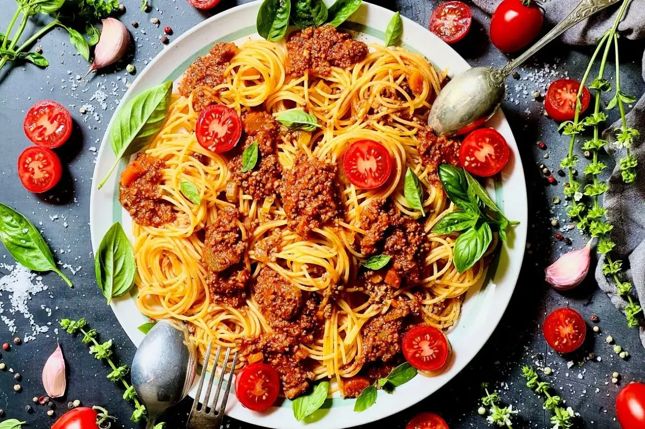 Ein Teller Spaghetti Bolognese, garniert mit frischen Tomaten und Basilikum. Das ist, was bedeutet Bolognese: ein herzhaftes Gericht!