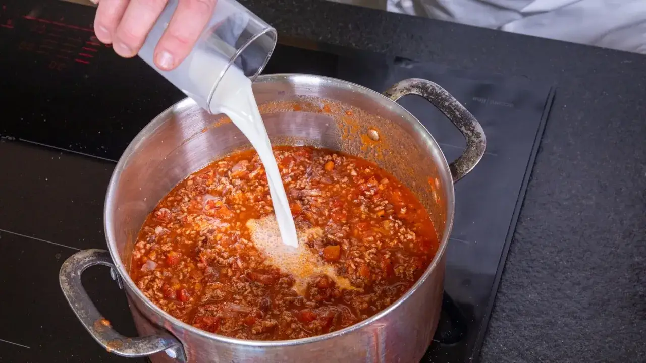 Milch wird in einen Topf mit k&ouml;chelnder Bolognese gegossen, um die Sauce cremiger zu machen.