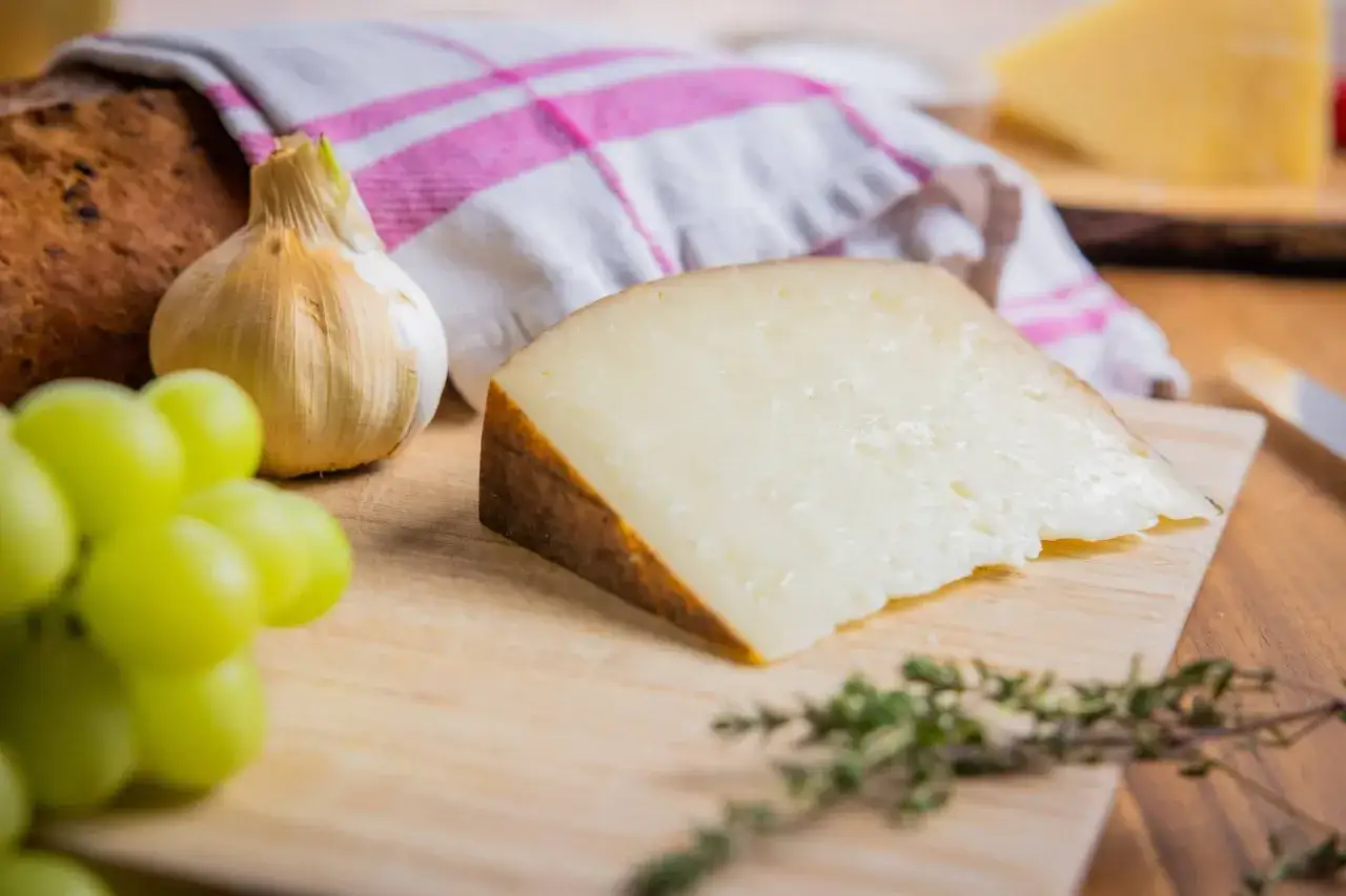 Ein Stück Pecorino, ein Hartkäse aus Schafsmilch, liegt neben Trauben, Knoblauch und Brot.
