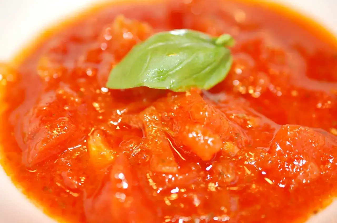 Eine Nahaufnahme von Marcella Hazan Tomatensauce mit einem frischen Basilikumblatt.