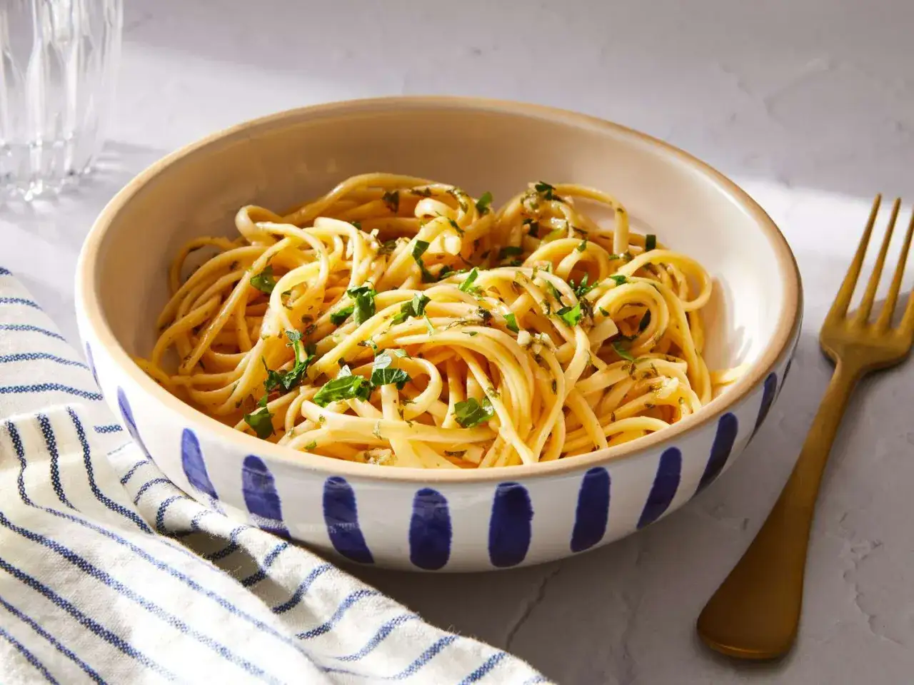 Eine Schüssel mit köstlichen linguini nudeln, garniert mit frischen Kräutern. Daneben liegt eine goldene Gabel.