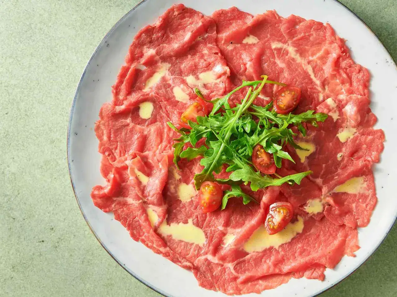 Carpaccio selber machen: hauchdünne Rinderfiletscheiben mit Rucola und Kirschtomaten, beträufelt mit einer cremigen Sauce.