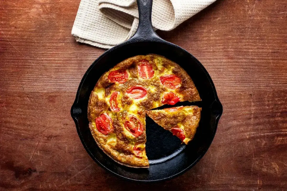 Eine goldbraune Tomaten-Frittata mit saftigen Tomatenscheiben, frisch aus der Gusseisenpfanne auf rustikalem Holztisch.