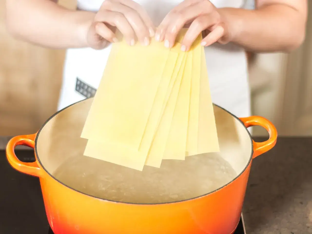 Hände halten Lasagneplatten über kochendes Wasser, um sie vorzukochen, ohne dass sie verkleben.