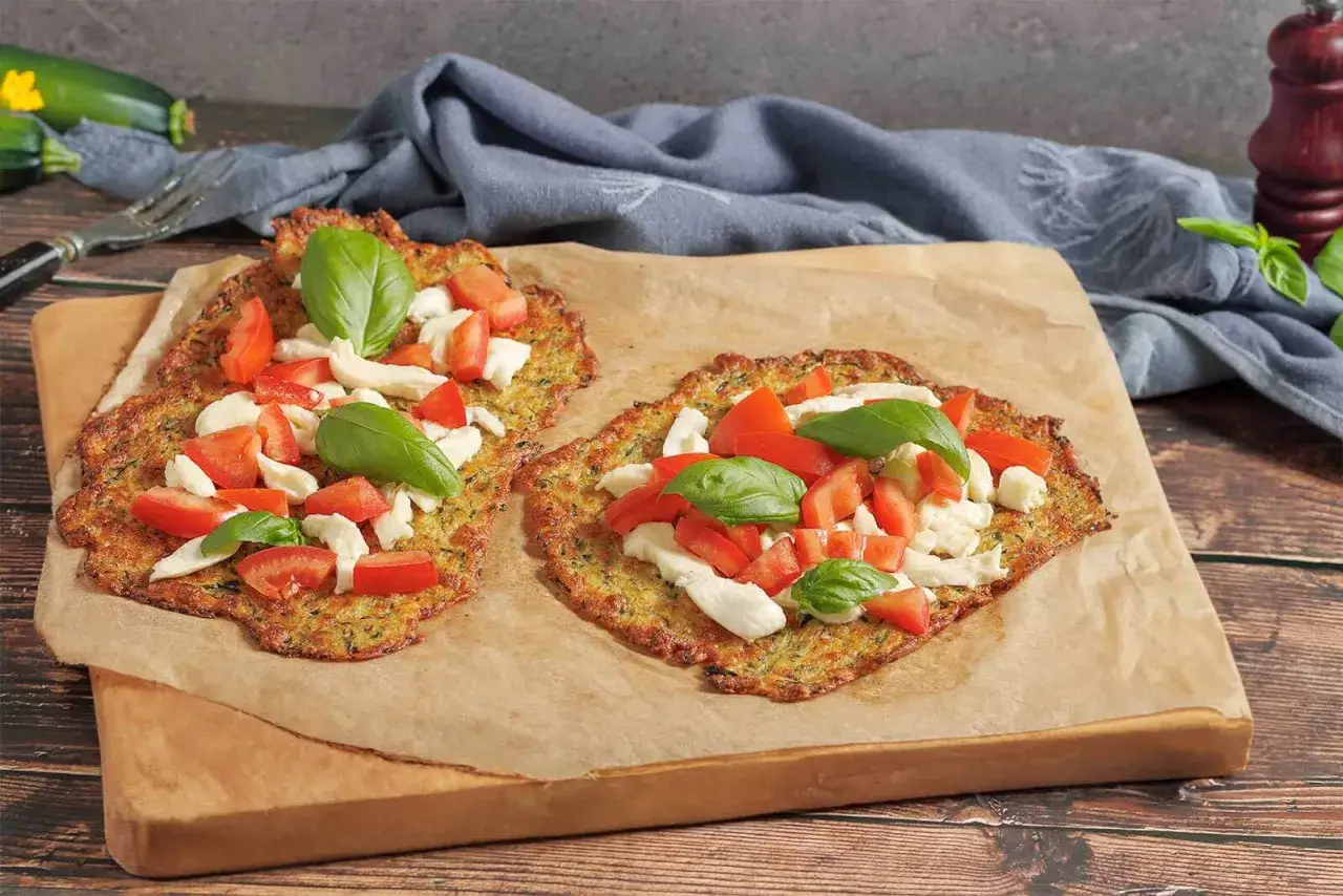 Zwei knusprige Zucchini-Pizzen mit Mozzarella, Tomaten und Basilikum auf Backpapier.