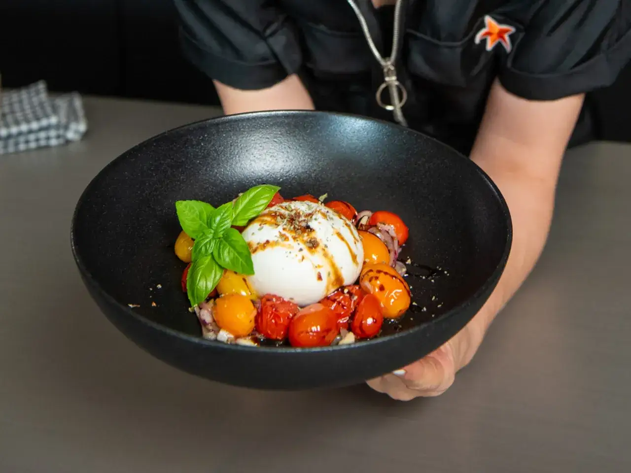 Burrata Caprese mit bunten Tomaten, Basilikum und Balsamico-Dressing auf einem schwarzen Teller.