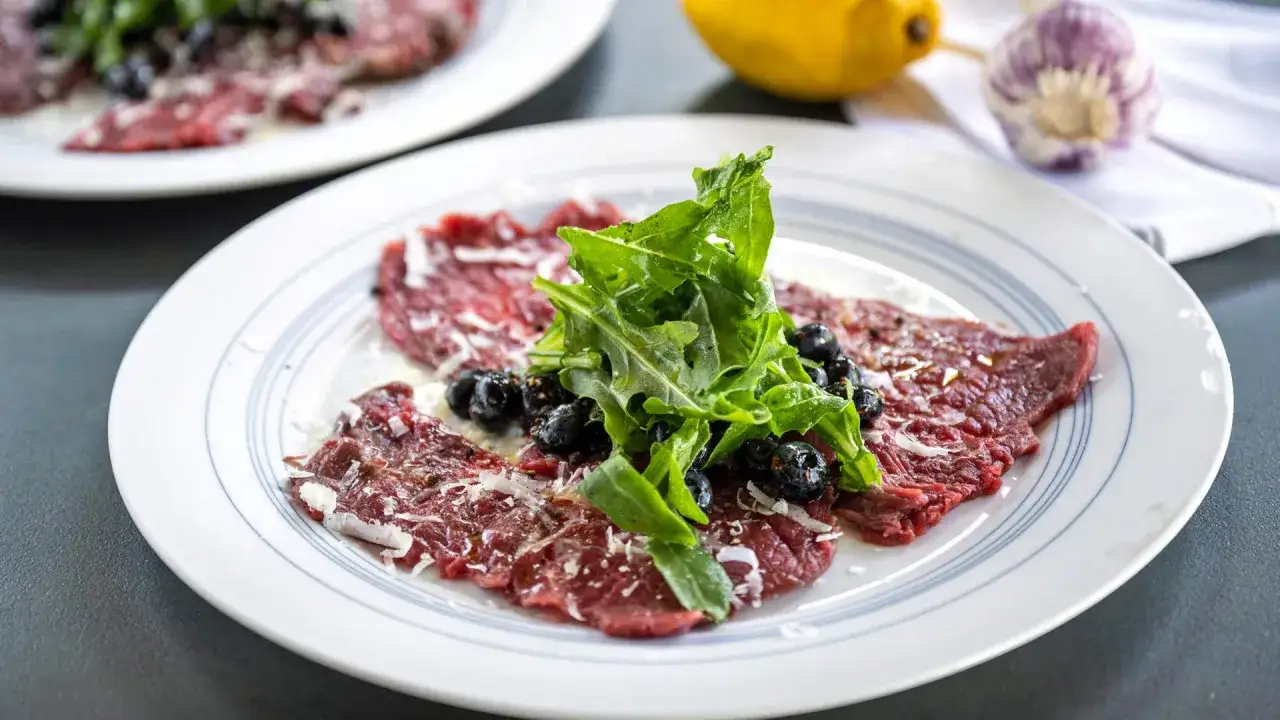 Carpaccio: hauchdünne Rindfleischscheiben mit Rucola, Blaubeeren und Parmesan. Ein leichter Genuss, der zeigt, was Carpaccio ist.