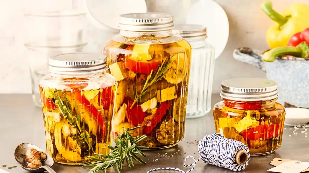Drei Gläser mit italienischem Fingerfood: eingelegte Paprika, Zucchini und Kräuter in Öl. Perfekt für Antipasti.