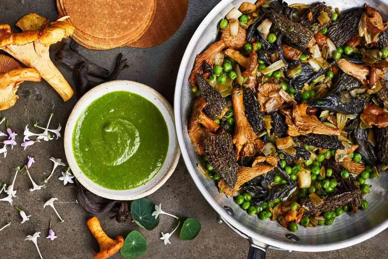Pfanne voller gebratener Pilze, Erbsen und Lauch, daneben eine Sch&uuml;ssel mit gr&uuml;ner Sauce und frische Kr&auml;uter. Ein Festmahl al funghi.