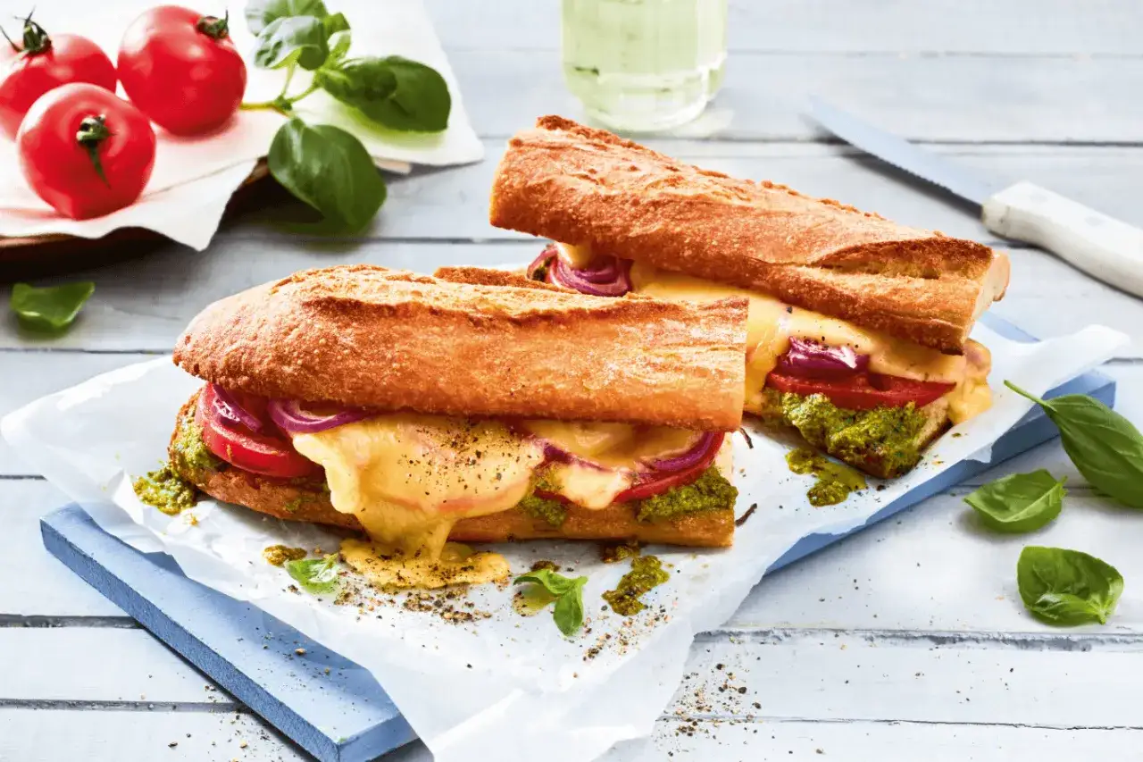 Zwei Baguette-Sandwiches mit geschmolzenem Käse, Tomaten, roten Zwiebeln und Pesto. So verwendet man Pesto für einen köstlichen Snack!