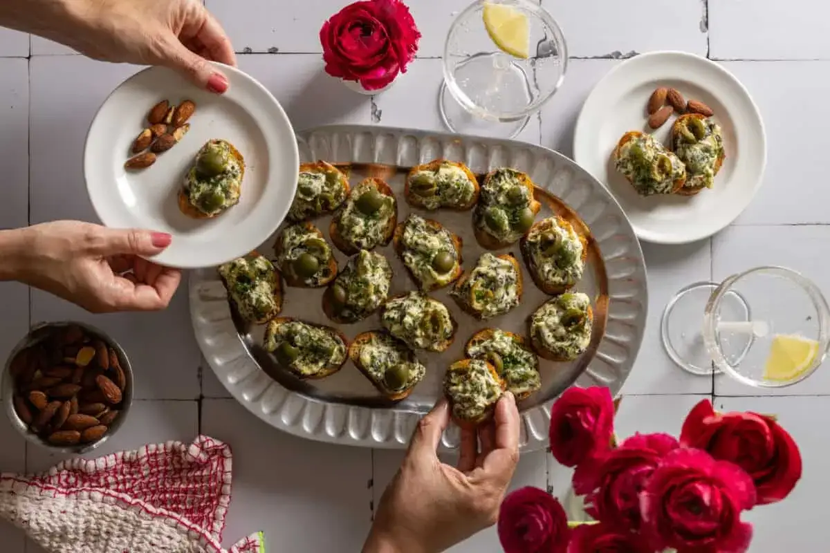 Köstliche Bruschetta mit Olivencreme, perfekt für ein einfaches olivencreme rezept. Mandeln und Blumen garnieren die Szene.