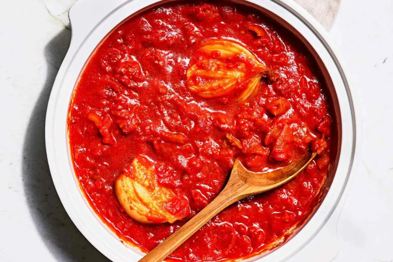 Tomatensoße mit Zwiebelstücken und einem Holzlöffel, wie in Marcella Hazan Rezepten üblich.