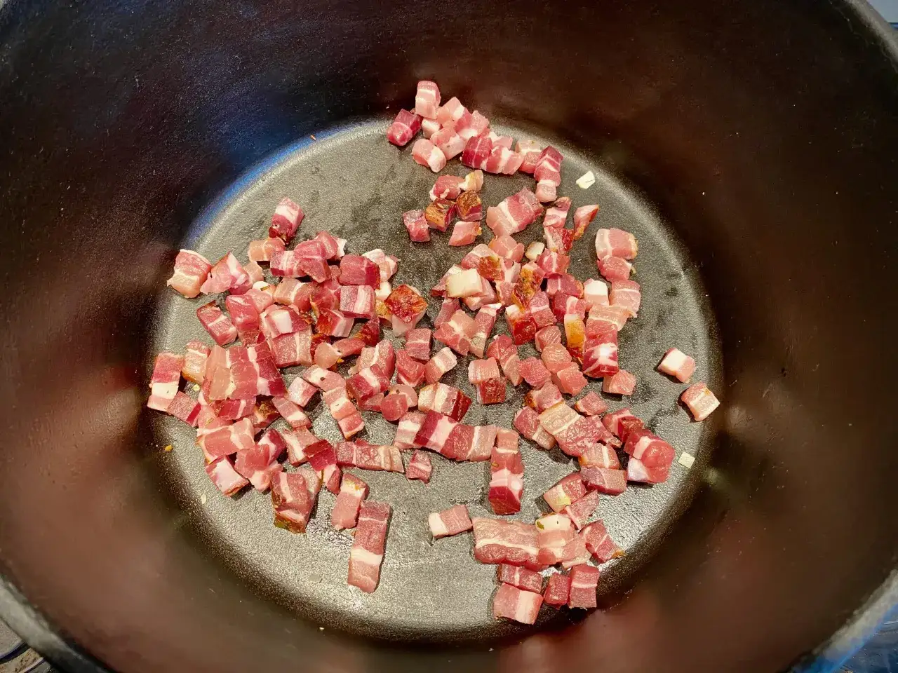 Würfel von Pancetta liegen in einem schwarzen Topf, bereit für eine herzhafte Bolognese.