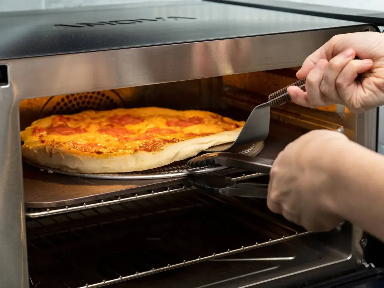 Eine Pizza mit Sourdough-Teig wird mit einem Pizzaschieber aus dem Ofen genommen.