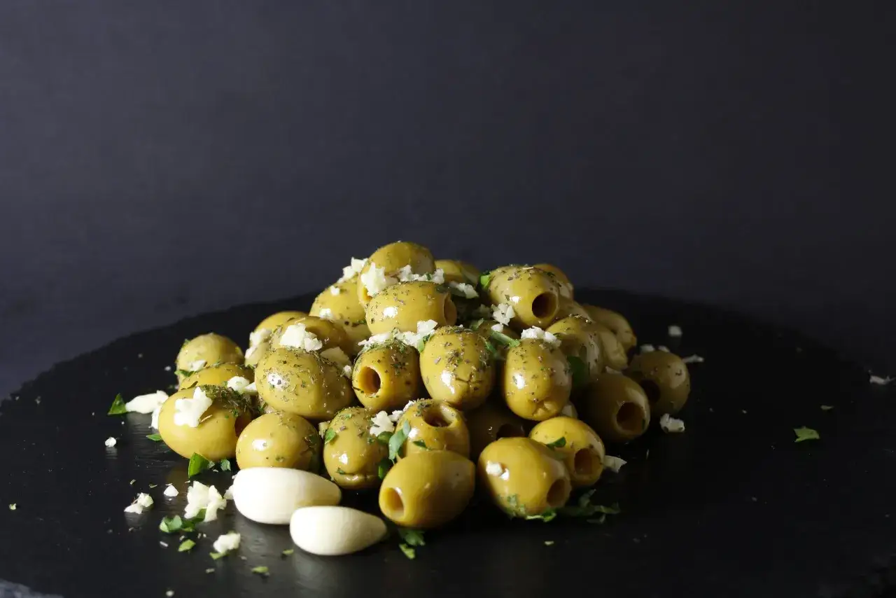 Ein Haufen grüner Oliven, bestreut mit gehacktem Knoblauch und Kräutern, bereit zum Braten.