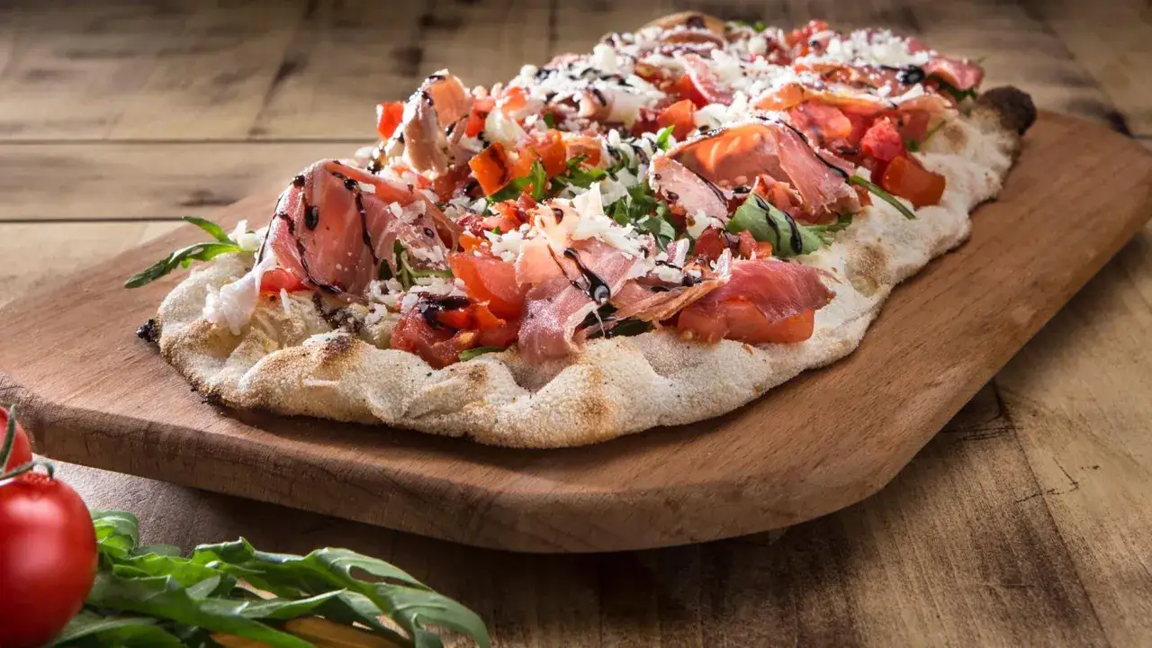 Leckeres Pinsa Rezept mit Prosciutto, Tomaten und Rucola, beträufelt mit Balsamico-Glasur.