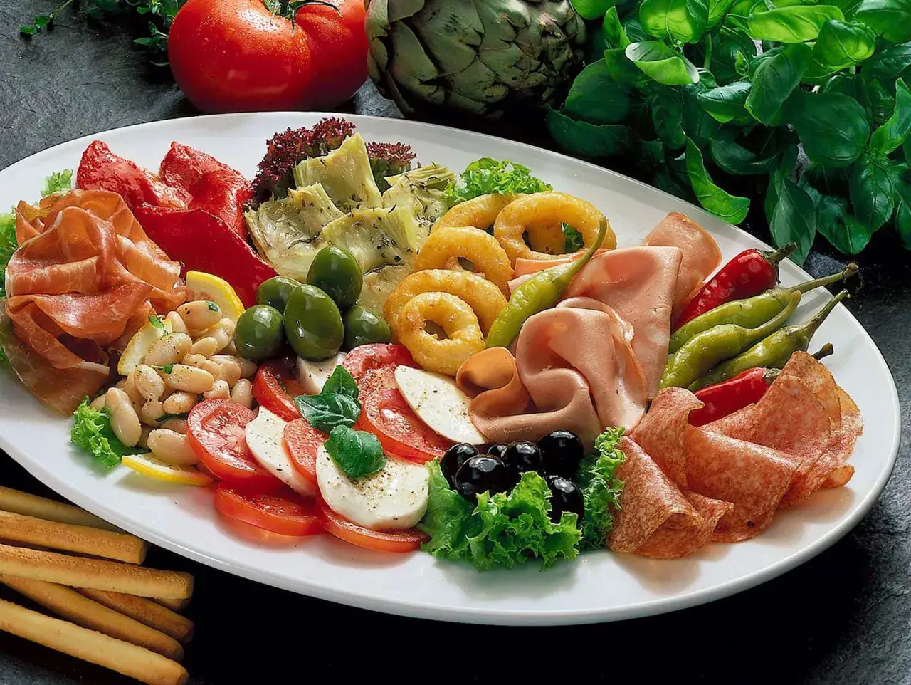 Bunte Antipasti-Platte mit Mozzarella-Tomaten-Scheiben, Schinken, Salami, Oliven und Artischocken – perfekt für leichte Mozzarella Rezepte kalt.