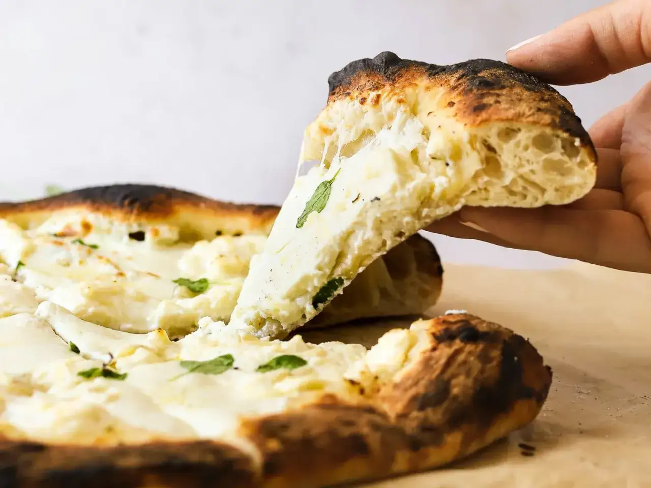 Eine handgehobene Scheibe Biancaneve Pizza mit geschmolzenem Käse und Kräutern.