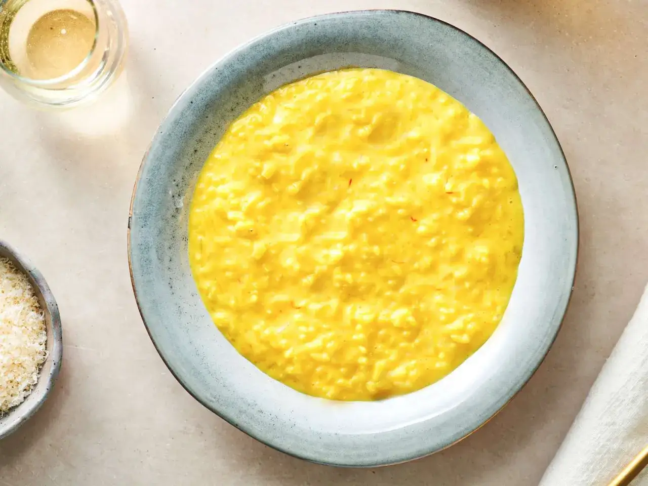 Cremiges, gelbes Risotto mit Safranfäden, perfekt als Risotto Grundrezept. Daneben geriebener Parmesan und ein Glas Weißwein.
