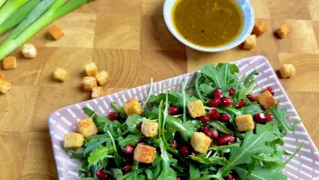 Frischer Rucola Salat mit Granatapfelkernen und Croutons, dazu ein Dressing.