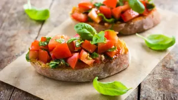 Zwei Bruschetta mit frischen Tomaten und Basilikum, garniert mit einem Hauch von Paprika, auf rustikalem Holz.