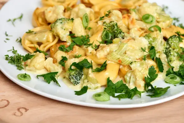 Tortellini mit Brokkoli und Blumenkohl in cremiger Sauce, garniert mit Petersilie. Lecker, wenn man Tortellini anbraten möchte.