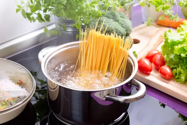 Spaghetti kochen in sprudelndem Wasser. Die richtige **Tagliatelle Kochzeit** ist entscheidend für ein perfektes Pastagericht. Frisches Gemüse wie Brokkoli, Karotten und Tomaten liegen bereit.