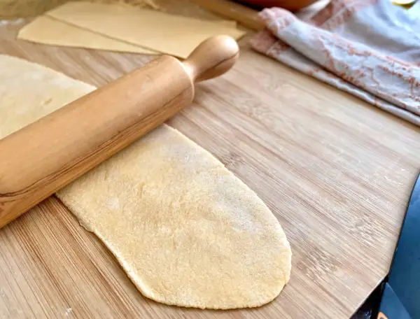 Mit einem Nudelholz wird Teig für **ravioli selber machen ohne maschine** auf einem Holzbrett ausgerollt.