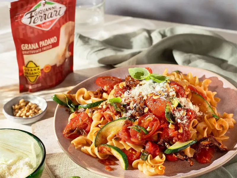 Fusilli mit Tomaten, Zucchini und Pinienkernen, bestreut mit frisch geriebenem Grana Padano. Perfekte parmesan verwendung für ein leichtes Gericht.