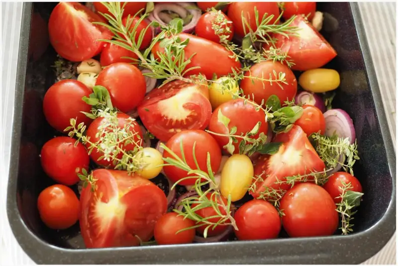 Tomaten einkochen im Backofen: Frische Tomaten, Zwiebeln und Kräuter in einer Auflaufform, bereit für den Ofen.