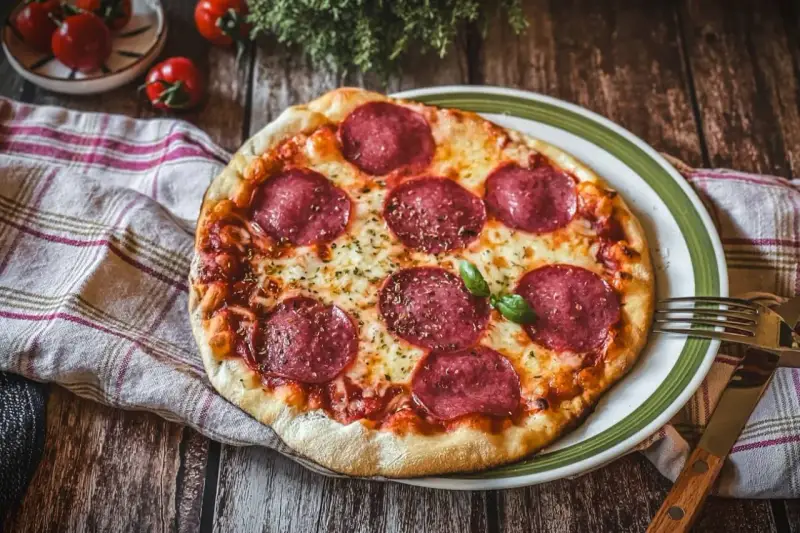 Eine köstliche Pizza Salami mit geschmolzenem Käse und frischem Basilikum auf einem rustikalen Holztisch.
