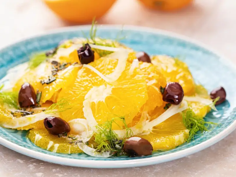 Erfrischender orangensalat sizilianisch mit Fenchel und dunklen Oliven auf einem blauen Teller.